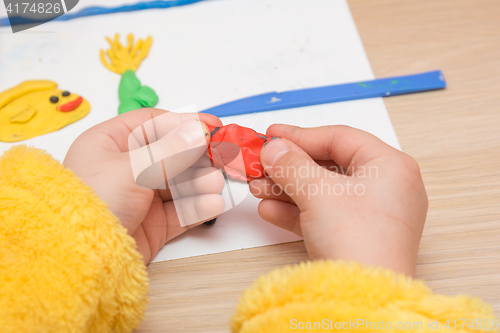 Image of The child is holding a piece of red clay, close-up