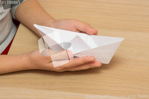 Image of The child holds in his hands a paper boat, close-up
