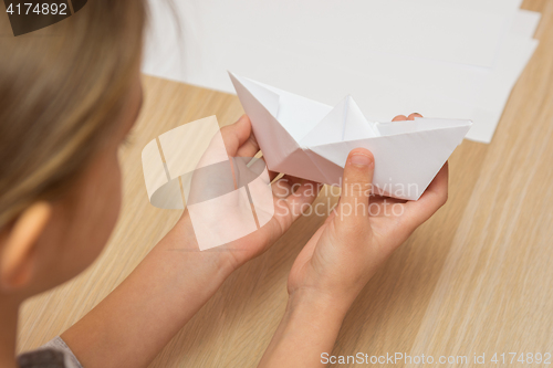 Image of A girl looks at a paper boat made by hand