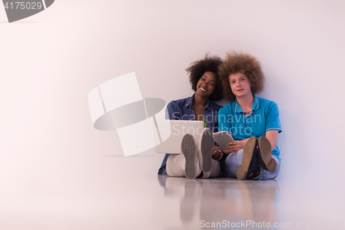 Image of multiethnic couple sitting on the floor with a laptop and tablet