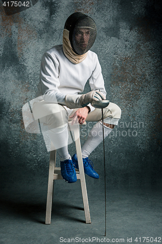 Image of The man wearing fencing suit with sword against gray