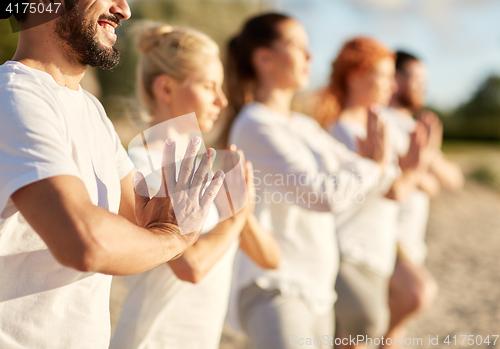 Image of group of people making yoga or meditating on beach