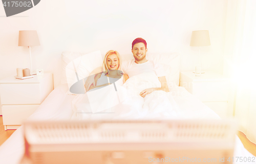 Image of happy couple lying in bed at home and watching tv