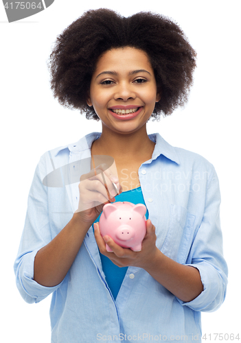 Image of happy african woman putting coin into piggy bank