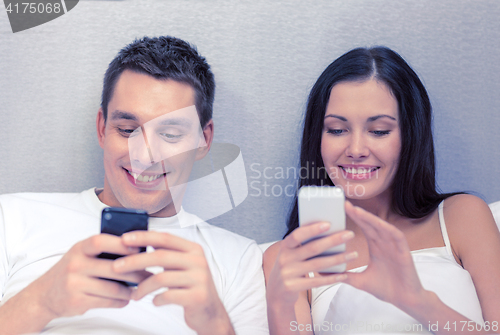 Image of smiling couple in bed with smartphones