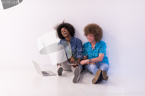 Image of multiethnic couple sitting on the floor with a laptop and tablet