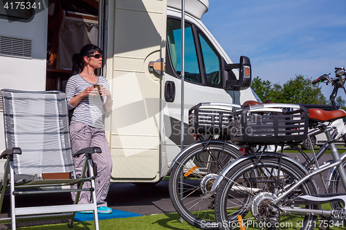 Image of Woman is standing with a mug of coffee near the camper.