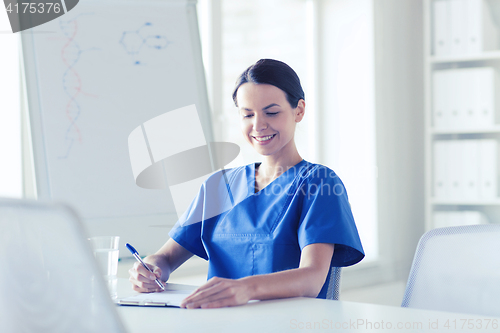 Image of happy female doctor or nurse writing to clipboard