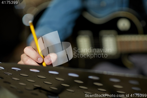 Image of man with guitar writing to music book at studio