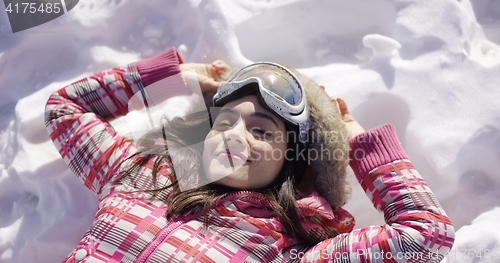Image of Young woman lying on snow with ski goggles
