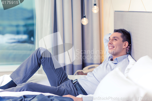 Image of happy businesswoman lying in bed in hotel room