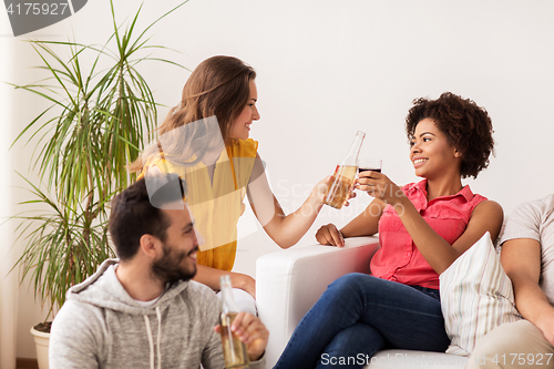 Image of happy friends clinking bottles of beer at home