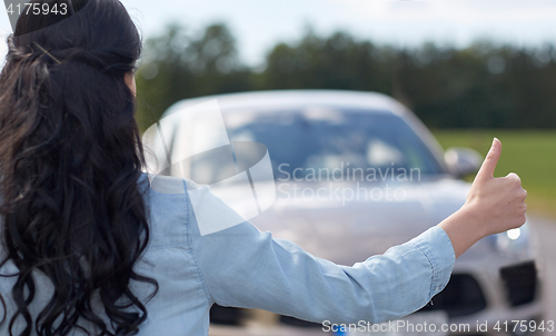 Image of woman hitchhiking and stopping car with thumbs up