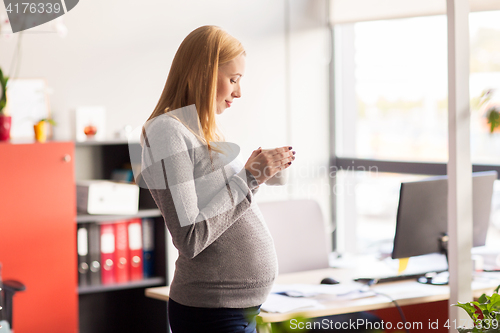 Image of pregnant businesswoman with cup of tea at office