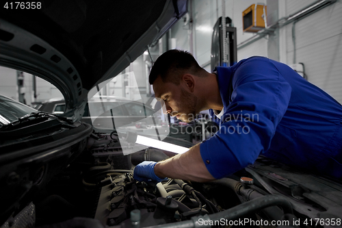 Image of mechanic man with lamp repairing car at workshop