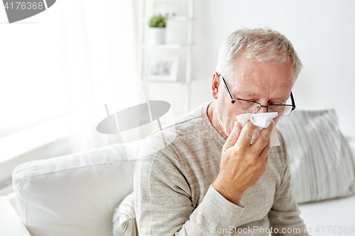 Image of sick senior man with paper wipe blowing his nose