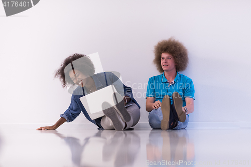 Image of multiethnic couple sitting on the floor with a laptop and tablet