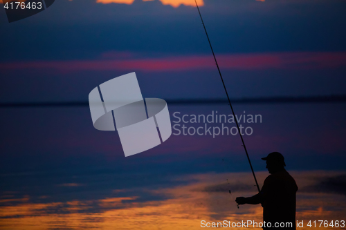 Image of Silhouette of fishermen on quiet ocean with rays sunset