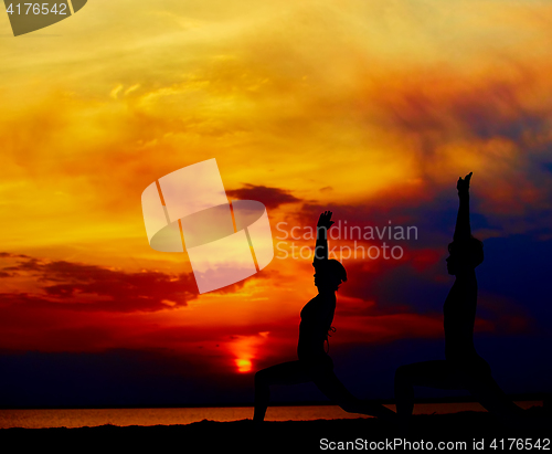 Image of Yoga people training and meditating in warrior pose outside by beach at sunrise or sunset.