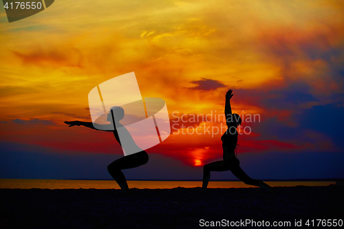 Image of Yoga people training and meditating in warrior pose outside by beach at sunrise or sunset.