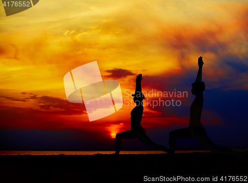 Image of Yoga people training and meditating in warrior pose outside by beach at sunrise or sunset.