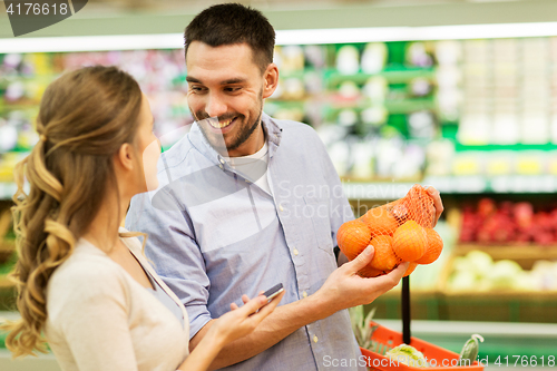 Image of happy couple buying oranges at grocery store