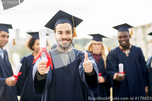 Image of happy students with diplomas showing thumbs up