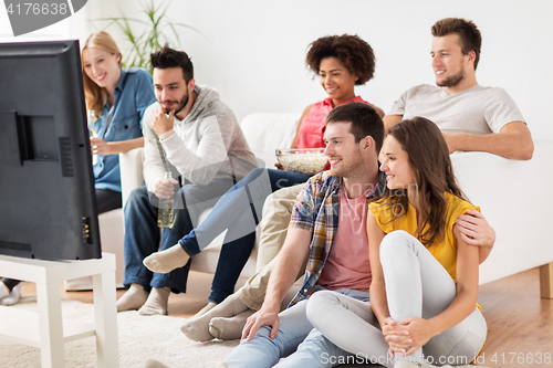 Image of happy friends with popcorn watching tv at home