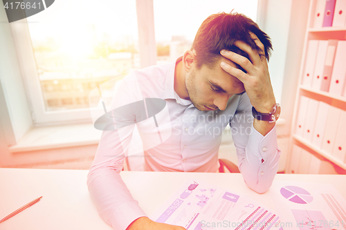 Image of stressed businessman with papers in office