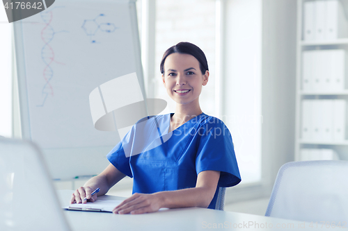 Image of happy female doctor or nurse writing to clipboard