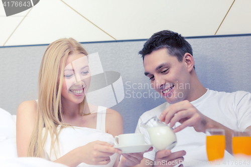 Image of smiling couple having breakfast in bed in hotel