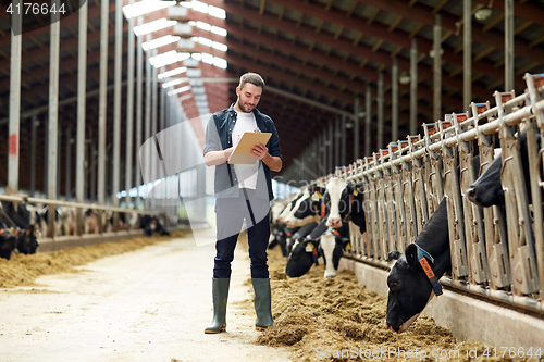 Image of farmer with clipboard and cows in cowshed on farm