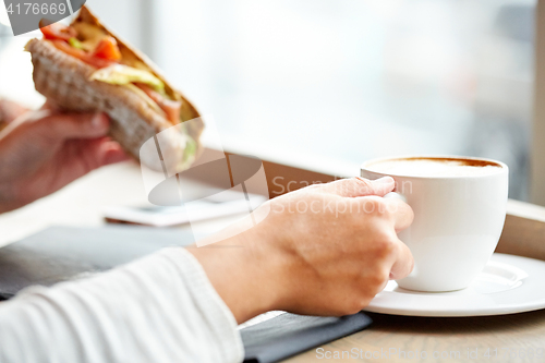 Image of woman drinking coffee and eating sandwich at cafe