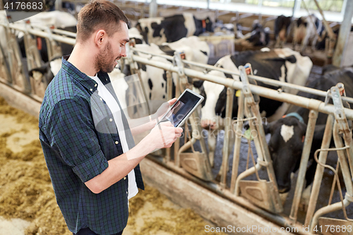 Image of young man with tablet pc and cows on dairy farm