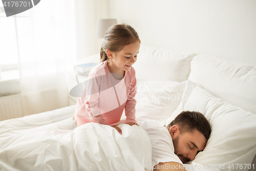 Image of little girl waking her sleeping father up in bed