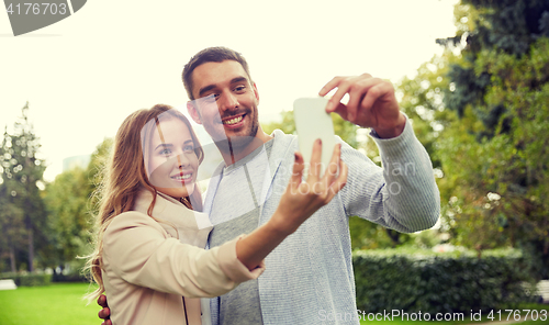 Image of happy couple with smartphone taking selfie in park