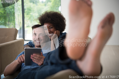 Image of multiethnic couple relaxing at  home with tablet computers
