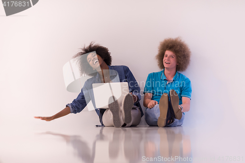 Image of multiethnic couple sitting on the floor with a laptop and tablet