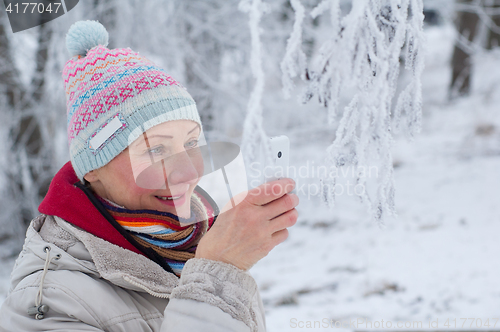 Image of Woman photographing on mobile phone in winter park