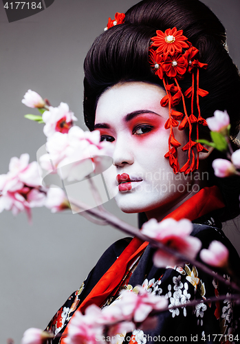 Image of young pretty geisha in black kimono among sakura, asian ethno close up