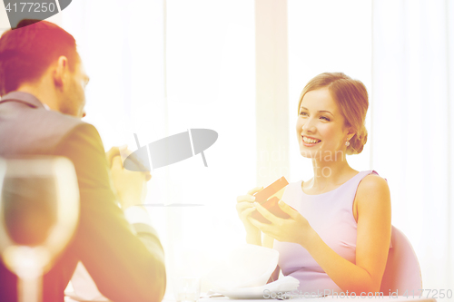 Image of excited young woman looking at boyfriend with box