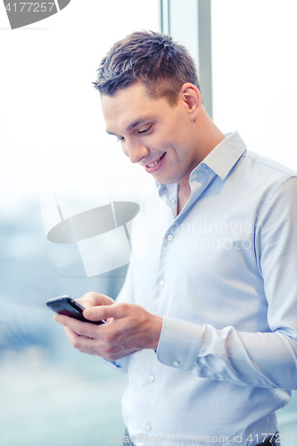 Image of smiling businessman with smartphone in office