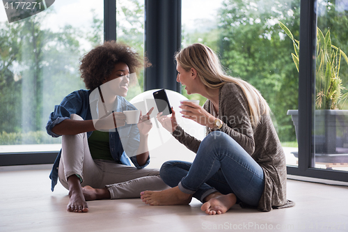 Image of multiethnic women sit on the floor and drinking coffee