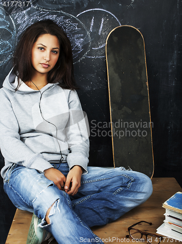 Image of young cute teenage girl in classroom at blackboard seating on ta