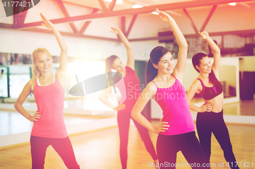 Image of group of smiling people stretching in the gym