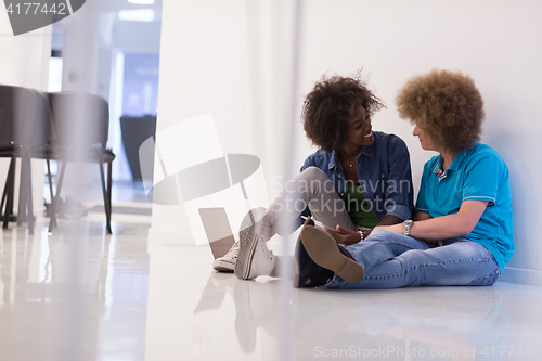 Image of multiethnic couple sitting on the floor with a laptop and tablet