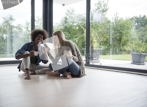 Image of multiethnic women sit on the floor and drinking coffee