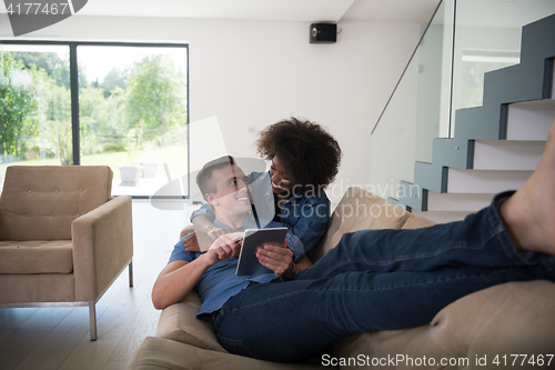 Image of multiethnic couple relaxing at  home with tablet computers