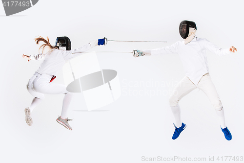 Image of The woman and man wearing fencing suit practicing with sword against gray