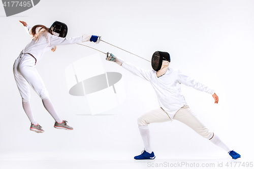 Image of The woman and man wearing fencing suit practicing with sword against gray